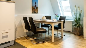 Ett modernt kök med mikrovågsugn, en matplats med bord och stolar, en målning av en fyr och ett fönster som släpper in naturligt ljus.