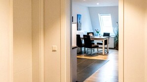 En hall som leder till ett matområde med ett bord och stolar, ett fönster och en växt.
