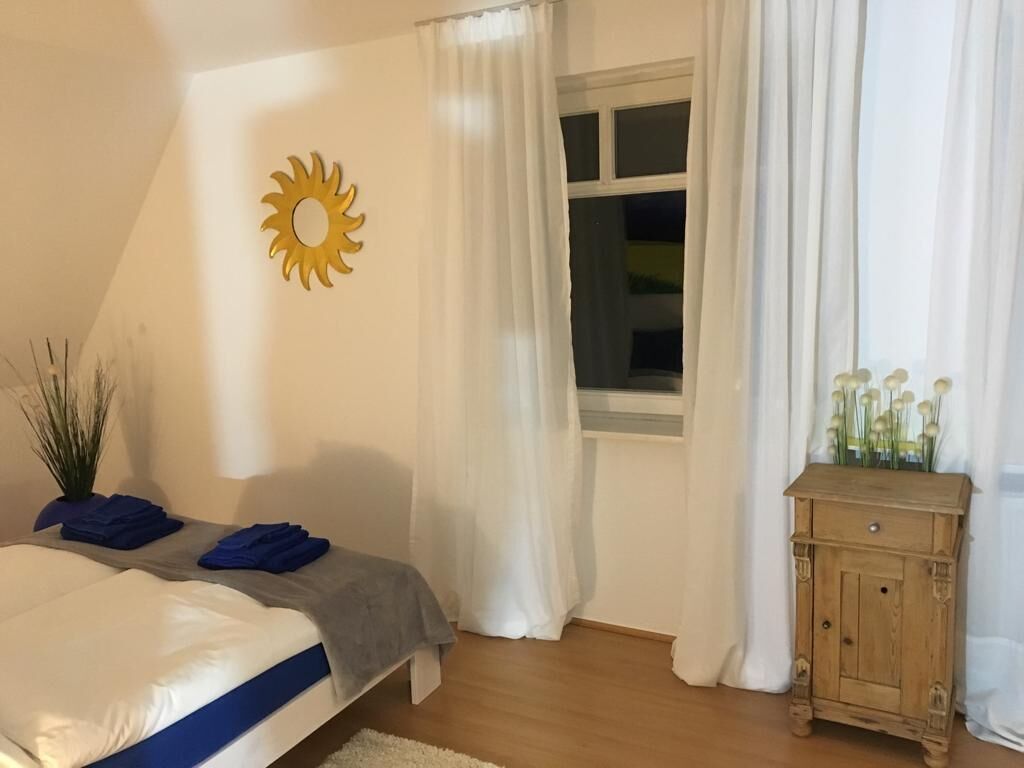Een slaapkamer met een bed, een raam met gordijnen, een houten kast en een zonversiering aan de muur.