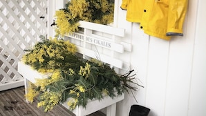 A white wooden bench with yellow flowers and greenery, a yellow jacket hanging on the wall, and a black boot on the floor.