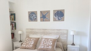 A bedroom with a bed, two bedside tables, a nightstand, a bookshelf, and three wall art pieces.