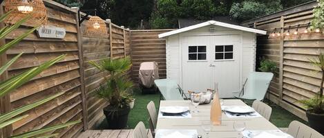 A wooden deck with a dining table set for four, surrounded by wooden fences and potted plants.