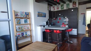 A modern kitchen with a central island, bar stools, and a wooden shelf with children's books. - T1 bis, view Nive, heart of city, ideal for couple / small family, everything on foot! (Bayonne)