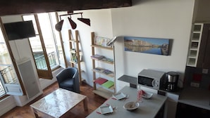 A compact living space with a dining table, a sofa, a bookshelf, a TV, and a kitchen area with a coffee maker. - T1 bis, view Nive, heart of city, ideal for couple / small family, everything on foot! (Bayonne)