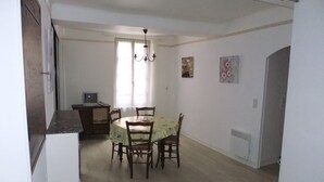 Un coin repas comprenant une table ronde, des chaises, un lustre et un téléviseur posé sur une petite table.