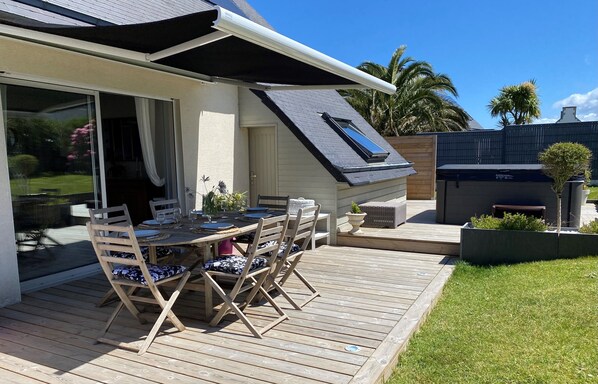 A modern house with a deck, a sliding glass door, and a small patio area with a table and chairs. - Spacious house with all comforts 500m from the beach! (Brittany)