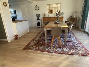 A dining area with a wooden table, chairs, and a patterned rug. A clock and a mirror are on the wall. - Spacious house with all comforts 500m from the beach! (Brittany)