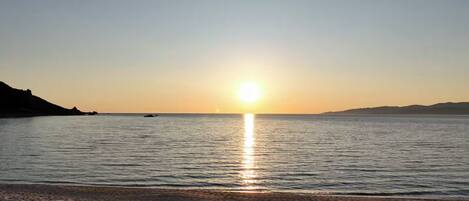A sunset over a calm sea with a beach in the foreground.
