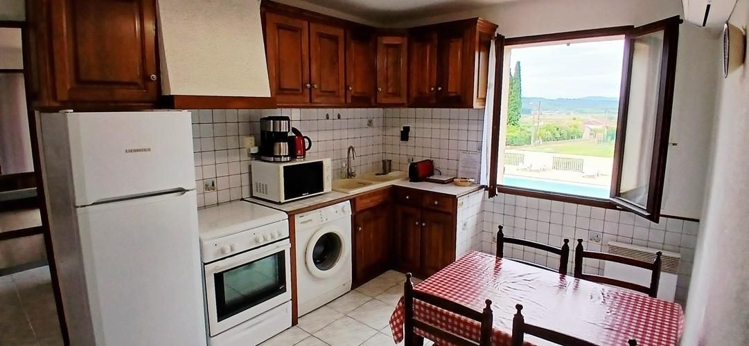 Eine kompakte Küche mit Holzschränken, einem Kühlschrank, einer Mikrowelle, einer Waschmaschine und einem Tisch mit kariertem Tischläufer.