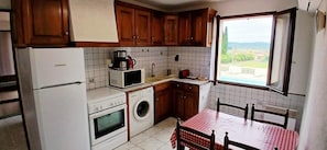A compact kitchen with wooden cabinets, a refrigerator, a microwave, a washing machine, and a table with a checkered tablecloth.