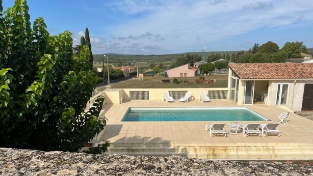 Ein Swimmingpool mit Liegestühlen, umgeben von einem Garten und Blick auf die Landschaft.