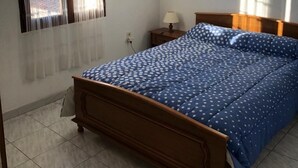 Ein Schlafzimmer mit einem hölzernen Bett, einem Nachttisch, einer Lampe und einem Fenster mit Vorhängen.
