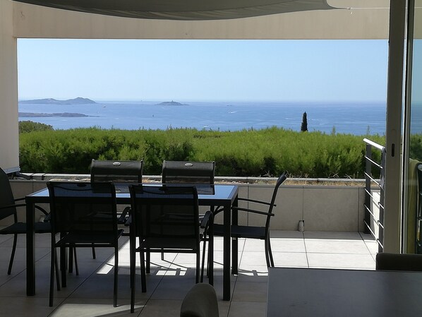 Um pátio externo com mesa e cadeiras, com vista para o mar e ilhas distantes.