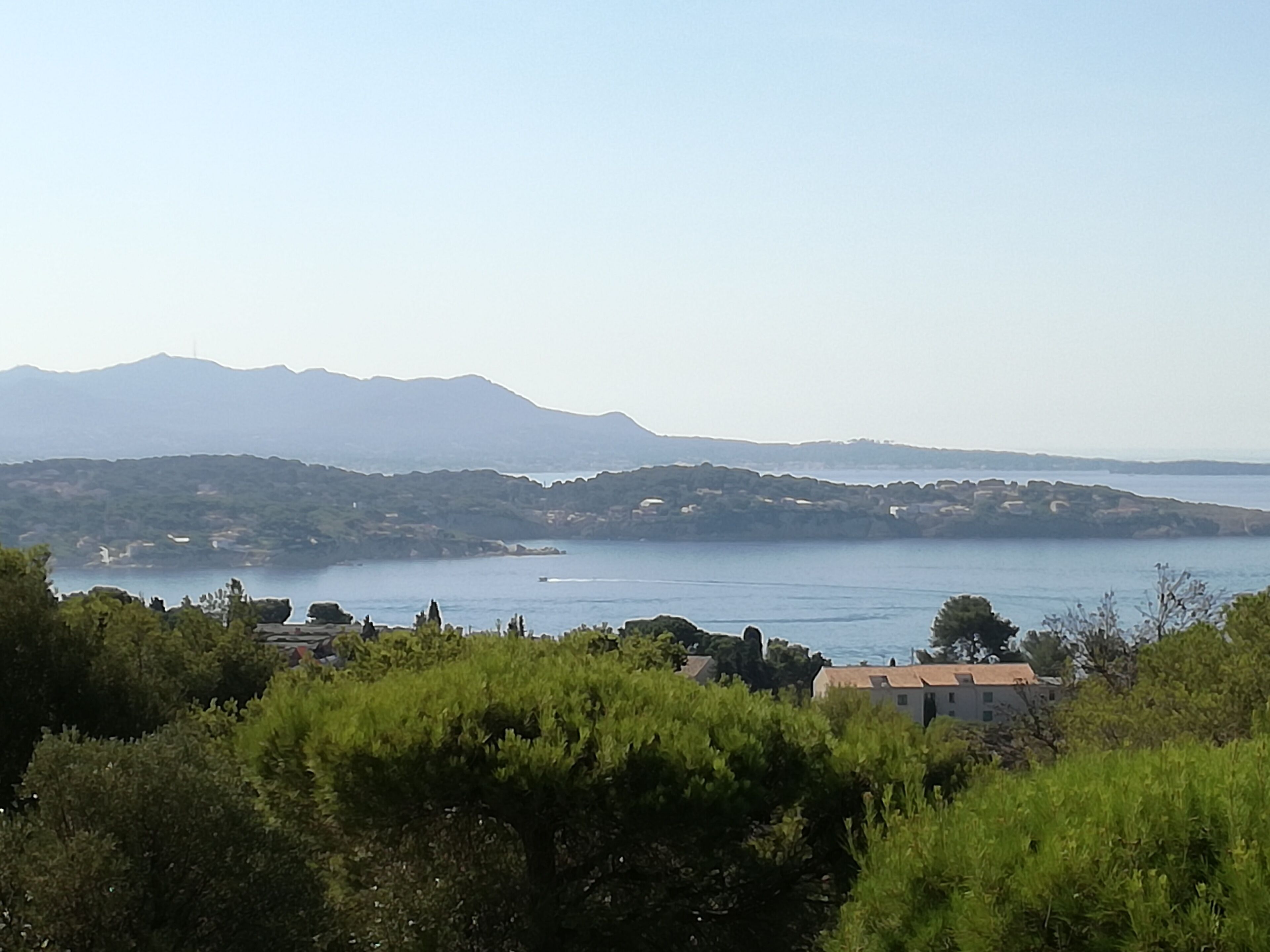 Un paisaje costero con vista despejada al mar, montañas distantes y un edificio con techo rojo en primer plano.
