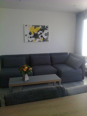 Uma sala moderna com um sofá cinza escuro, uma mesa de centro de madeira com um vaso de flores e um grande quadro abstrato na parede.