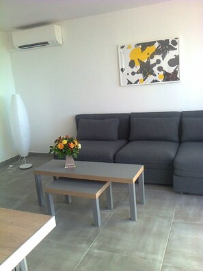 Uma sala de estar moderna com um sofá cinzento, uma mesa de centro de madeira e um vaso de flores.
