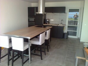 Cozinha moderna com ilha central, armários escuros e vista através de uma porta de vidro.