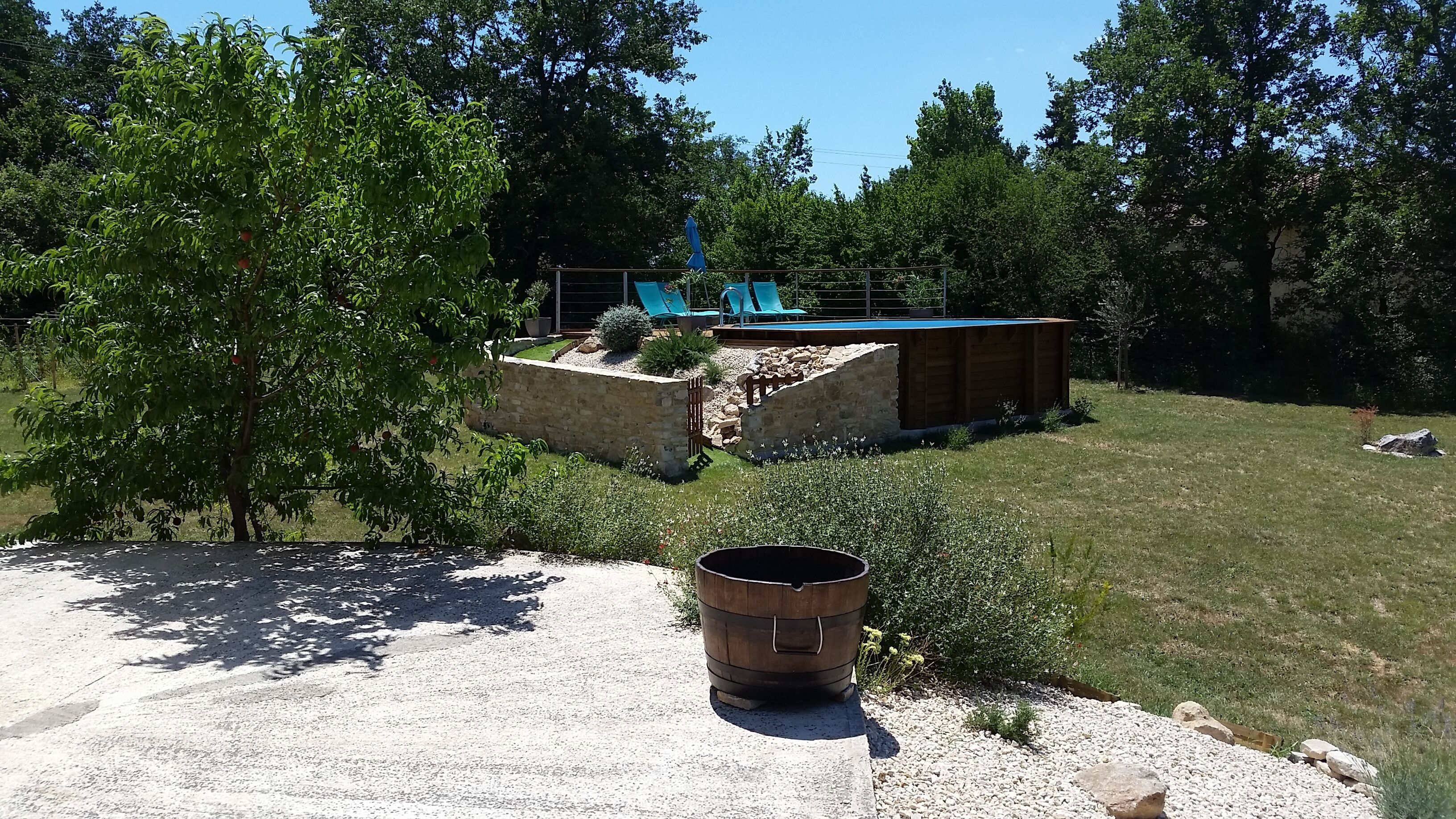 A backyard with a swimming pool, a wooden deck, and a stone wall.