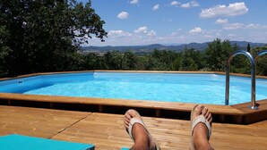 A wooden deck with a swimming pool, a person relaxing with feet propped up on the edge, and a scenic view of mountains and trees in the background. - Very nice Mazet with pool and panoramic views of the Cevennes (Saint-Privat-de-Champclos)