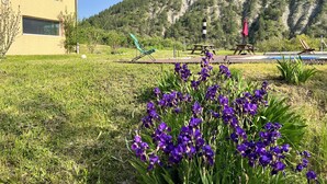 A building with a yellow facade, a grassy area with purple flowers, and a mountainous backdrop. - Large villa with swimming pool in a peaceful setting in the Baronnies provençales (Verclause)