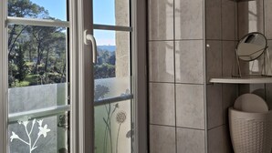 A bathroom with a large window, tiled walls, and a shelf with a mirror and basket.