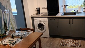 Een kleine keuken met een wasmachine, een koffiezetapparaat en een raam met uitzicht op bomen.