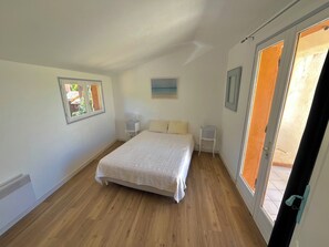Une chambre à coucher comprenant un lit, deux tables de chevet, une fenêtre et une porte donnant sur un espace extérieur.