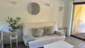 Een kamer met een witte bank, een kleine tafel, een potplant en een wandlamp.