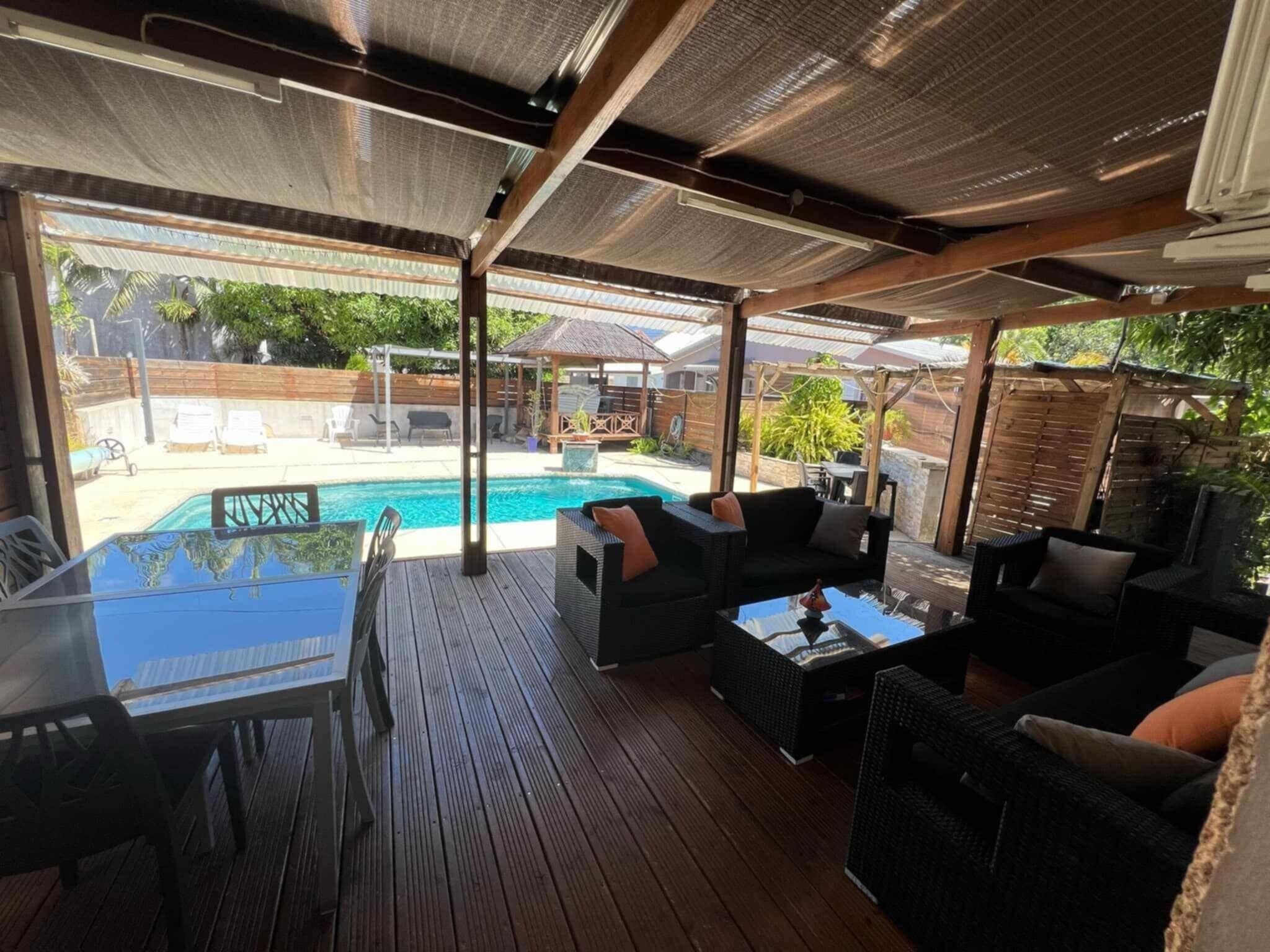 An outdoor patio with a pool, wooden deck, and outdoor furniture.