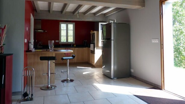 Une cuisine moderne dotée d’un grand îlot central, de tabourets de bar, d’un réfrigérateur et d’une fenêtre laissant entrer la lumière naturelle.