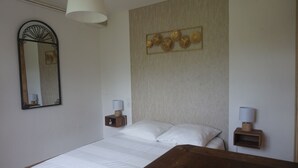 Een slaapkamer met een bed, twee nachtkastjes met lampen, een spiegel aan de muur en een decoratief paneel boven het bed.
