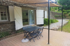 A stone building with a covered patio, a table and chairs, and a window with shutters. - Cévennes for rent Sumène (Sumène)