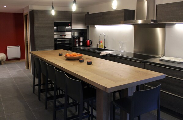 A modern kitchen with a wooden island, bar stools, stainless steel appliances, and a red accent wall.