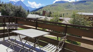 A balcony with a table and chairs, overlooking a mountainous landscape with buildings in the background.