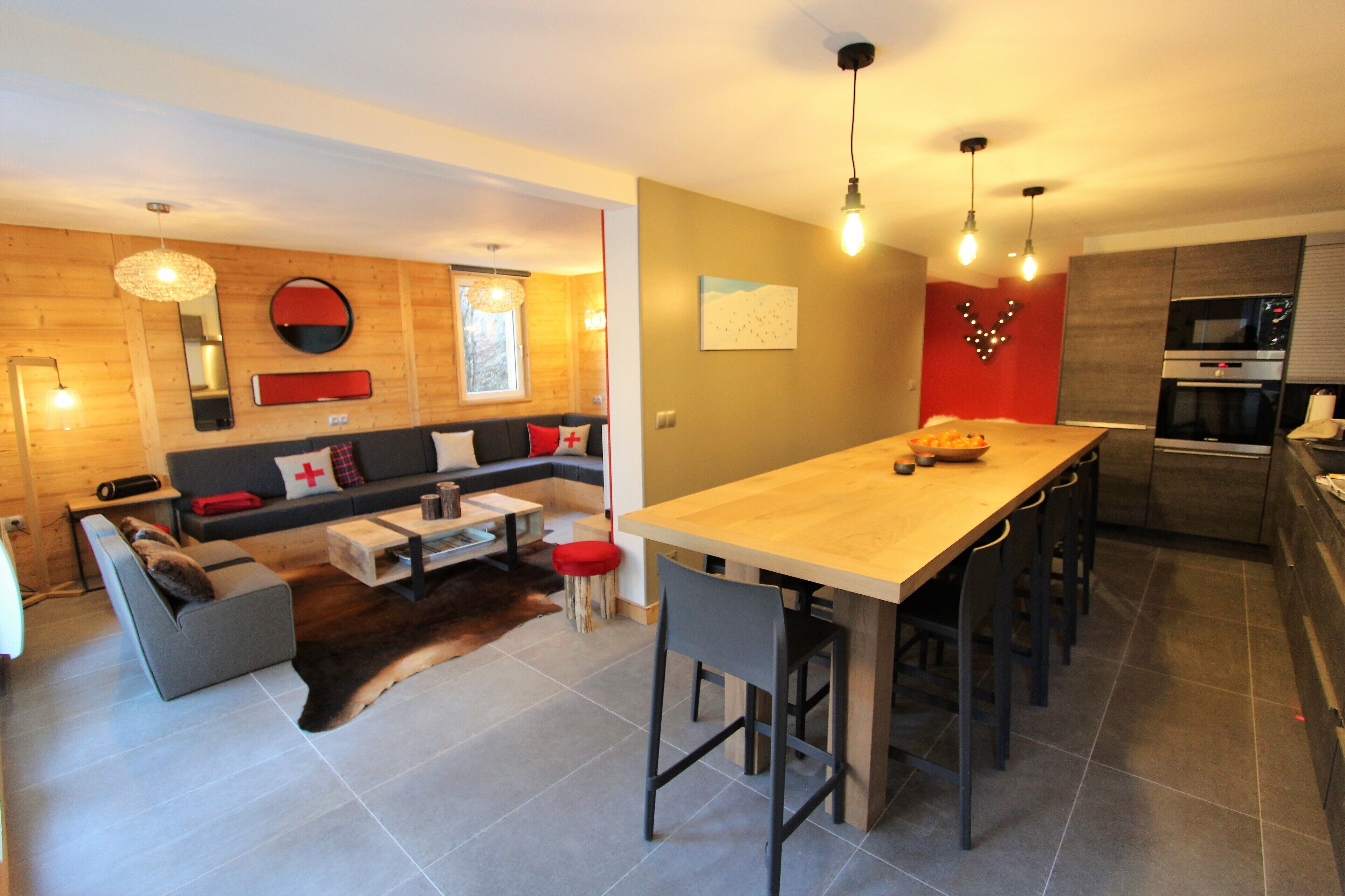 A modern kitchen with a wooden island and bar stools, a dining area with a sofa and a coffee table, and a living area with a sofa and a rug.