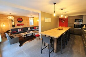 A modern kitchen with a wooden island and bar stools, a dining area with a sofa and a coffee table, and a living area with a sofa and a rug.