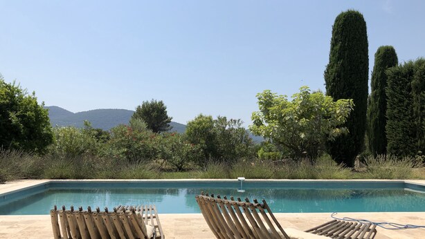 Ein Poolbereich mit zwei Holzliegen, freiem Blick auf Berge und einem gepflegten Garten.