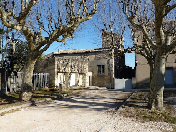 Une propriété rurale avec une allée de gravier menant à un bâtiment en pierre surmonté d’un toit en tuiles.