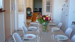 Un'area pranzo con tavolo apparecchiato per sei persone, sedie bianche e un vaso di fiori.