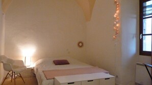 Una camera da letto con un letto, una sedia, un comodino, una cassettiera e una finestra decorata con luci a stringa.