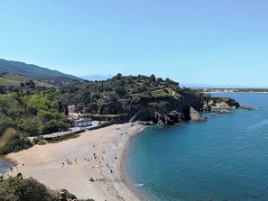 A coastal beach with rocky cliffs, clear blue water, and a few buildings in the background. - Charming house with garden and panoramic terrace; between sea and mountains! (Laroque-Des-Albères)