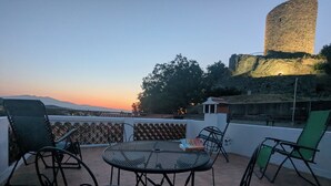 Een terras met een ronde tafel en stoelen, met uitzicht op een historische toren en verre bergen.