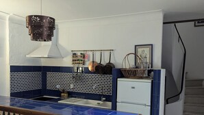 Een keuken met blauw-witte betegelde wanden, een witte koelkast, een hangende kruidenrek en een houten tafel met een decoratief blad.