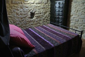 A single bed with a patterned blanket, a stone wall, and a dark door.