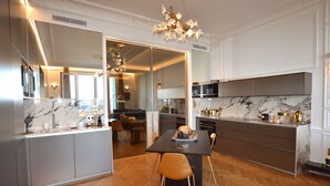 Une cuisine moderne avec des plans de travail en marbre, un coin repas avec une table et des chaises en bois, et un grand miroir qui agrandit visuellement l’espace.