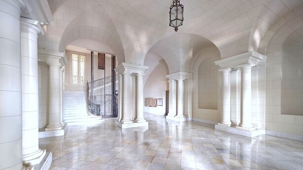 Un intérieur spacieux avec des colonnes blanches, un sol en marbre et un escalier menant aux niveaux supérieurs.