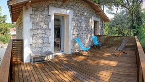 Una casa de piedra con terraza de madera, dos sillas azules y un banco.