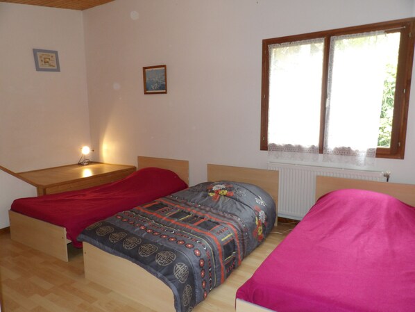 Un dormitorio con dos camas individuales, un escritorio de madera y una ventana con cortinas de encaje.
