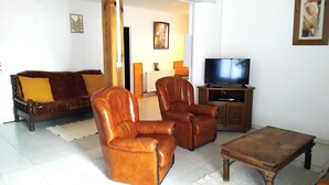 Ein Wohnzimmer mit einer Couch, zwei Ledersesseln, einem Couchtisch und einem Fernseher auf einem Holzboden.
