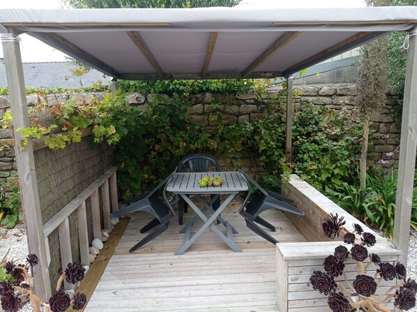 Un patio cubierto con una mesa y sillas, rodeado de muros de piedra y follaje.